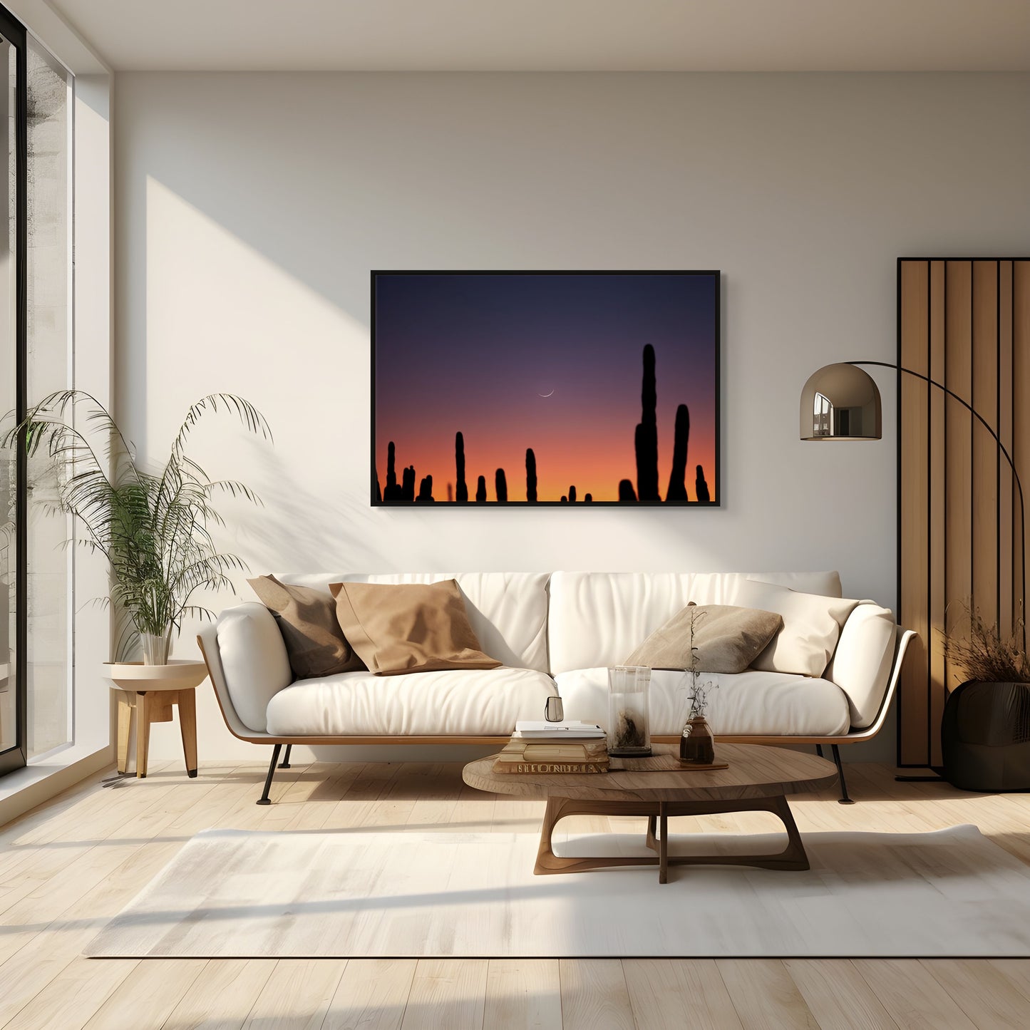 A black framed photograph of a crescent moon set behind a stand of cacti silhouettes in a modern room furnished with a couch, coffee table, lamp, and plant.