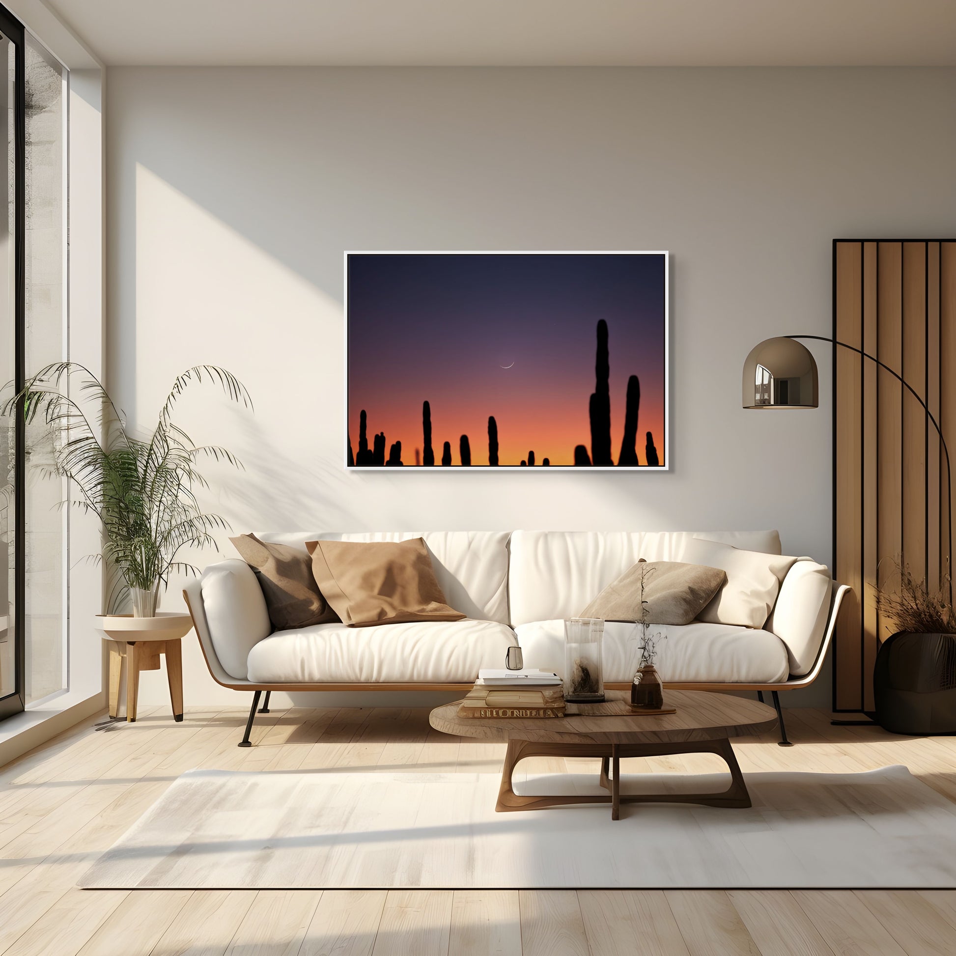 A white framed photograph of a crescent moon set behind a stand of cacti silhouettes in a modern room furnished with a couch, coffee table, lamp, and plant.