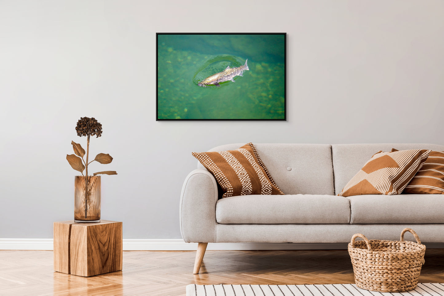 Living room with a sofa, decorative pillows, a plant, and a framed picture on the wall of a salmon rising to the surface of clear, green waters of a river pool. Black float frame.