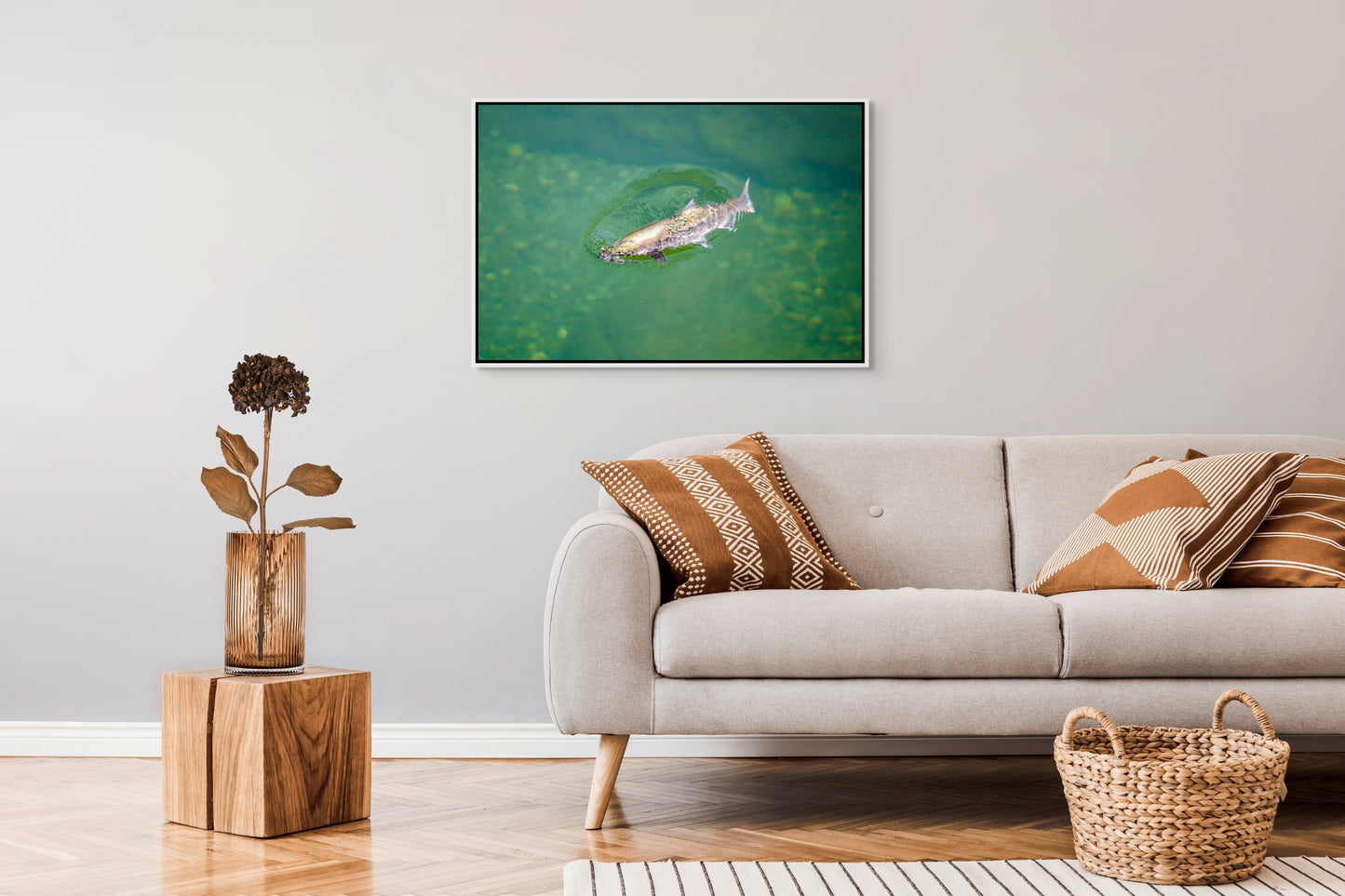 Living room with a sofa, decorative pillows, a plant, and a framed picture on the wall of a salmon rising to the surface of clear, green waters of a river pool. White float frame.