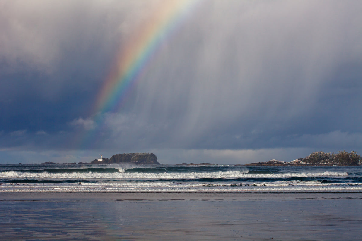 A rainbow and a downpour glide across Cox Bay on a snowy day in Tofino, BC.
