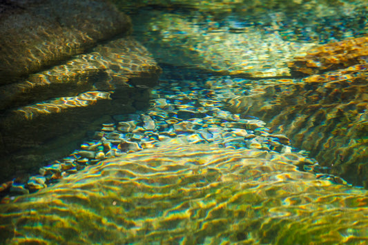 Clear water flowing over rocks with sunlight filtering through