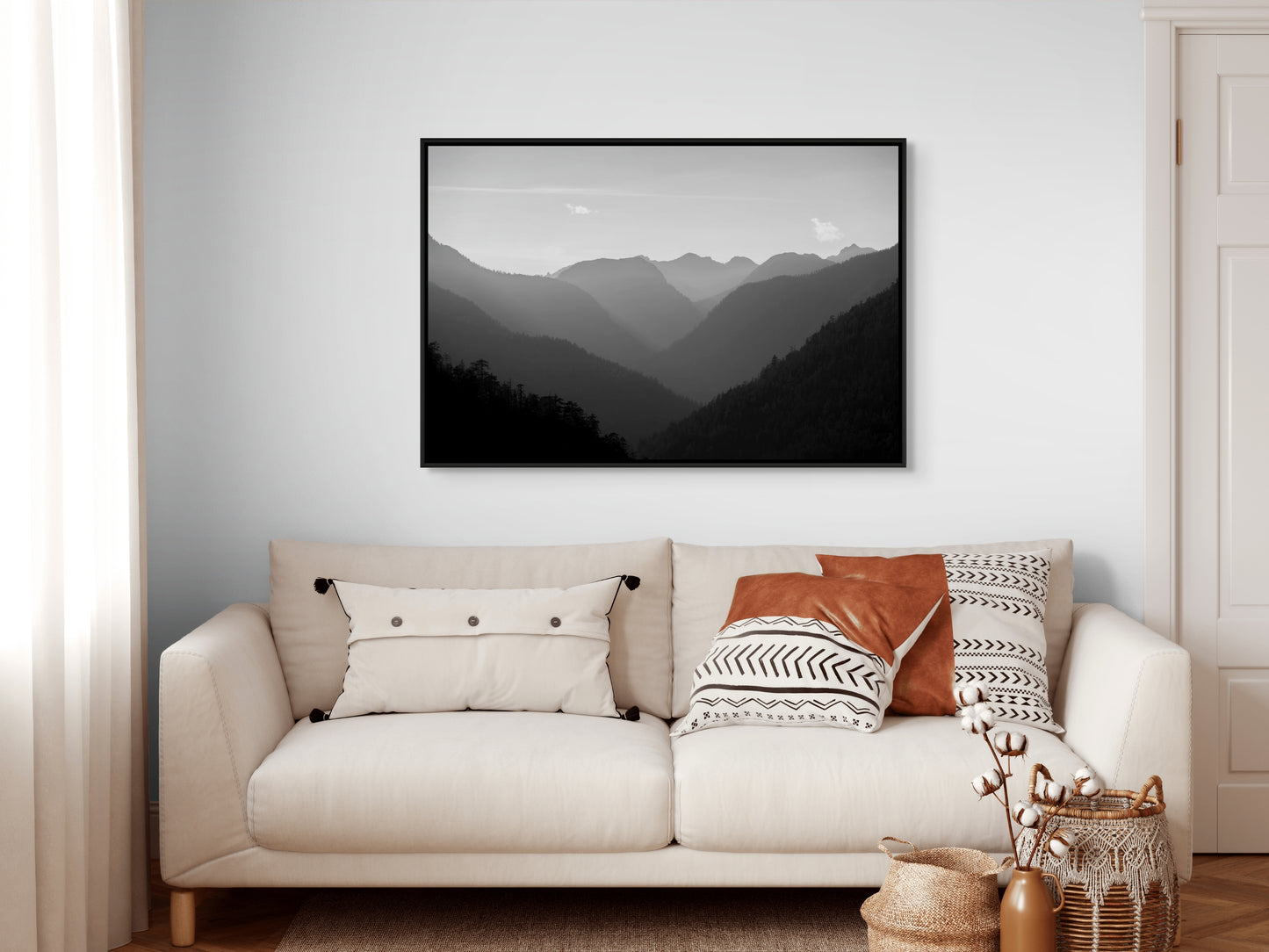 Beige sofa with decorative pillows and a black framed mountain landscape painting on a white wall.