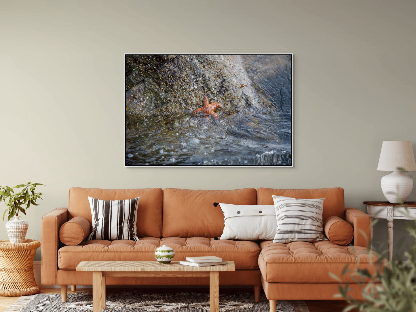 Living room with a orange sofa, coffee table, and decorative pillows, featuring a large white framed picture on the wall of a starfish resembling Patrick Star.