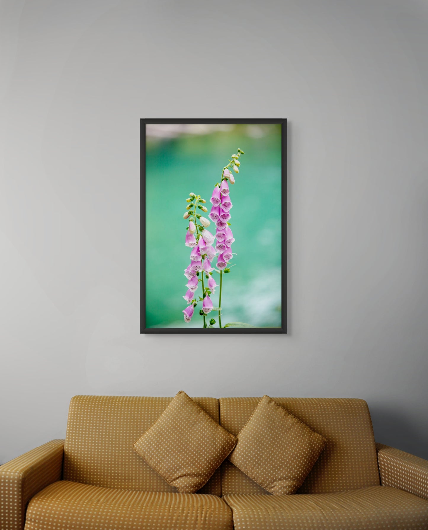 Black framed artwork of pink flowers on a gray wall above a brown sofa.