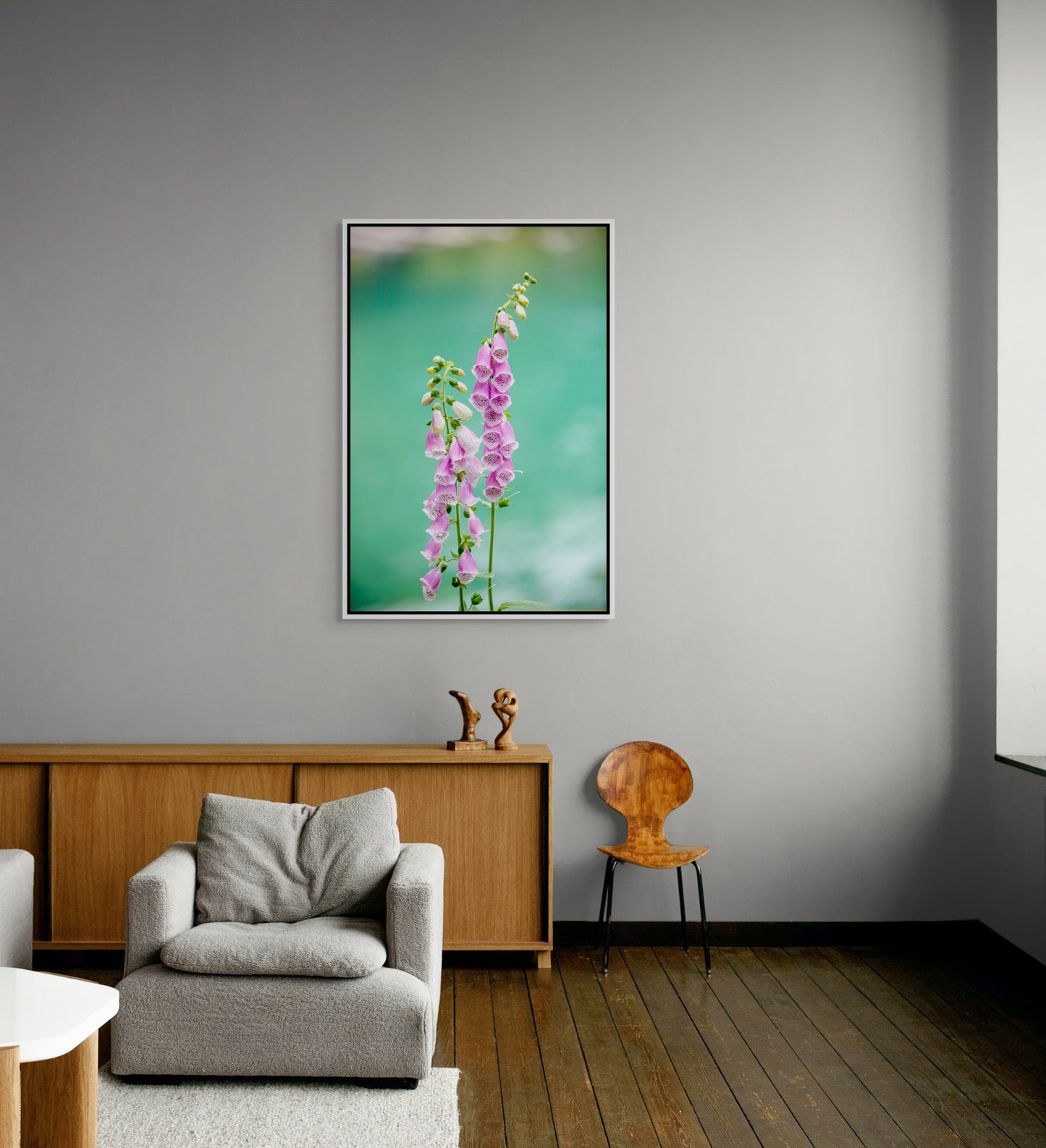 White framed floral artwork on a gray wall above a gray armchair and wooden sideboard.