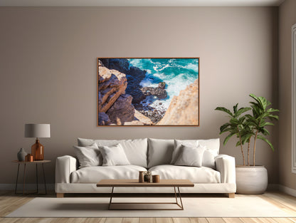 Modern living room with a white sofa, coffee table, tropical plant, and a cedar framed art print of a turquoise ocean meeting the rocky shore.