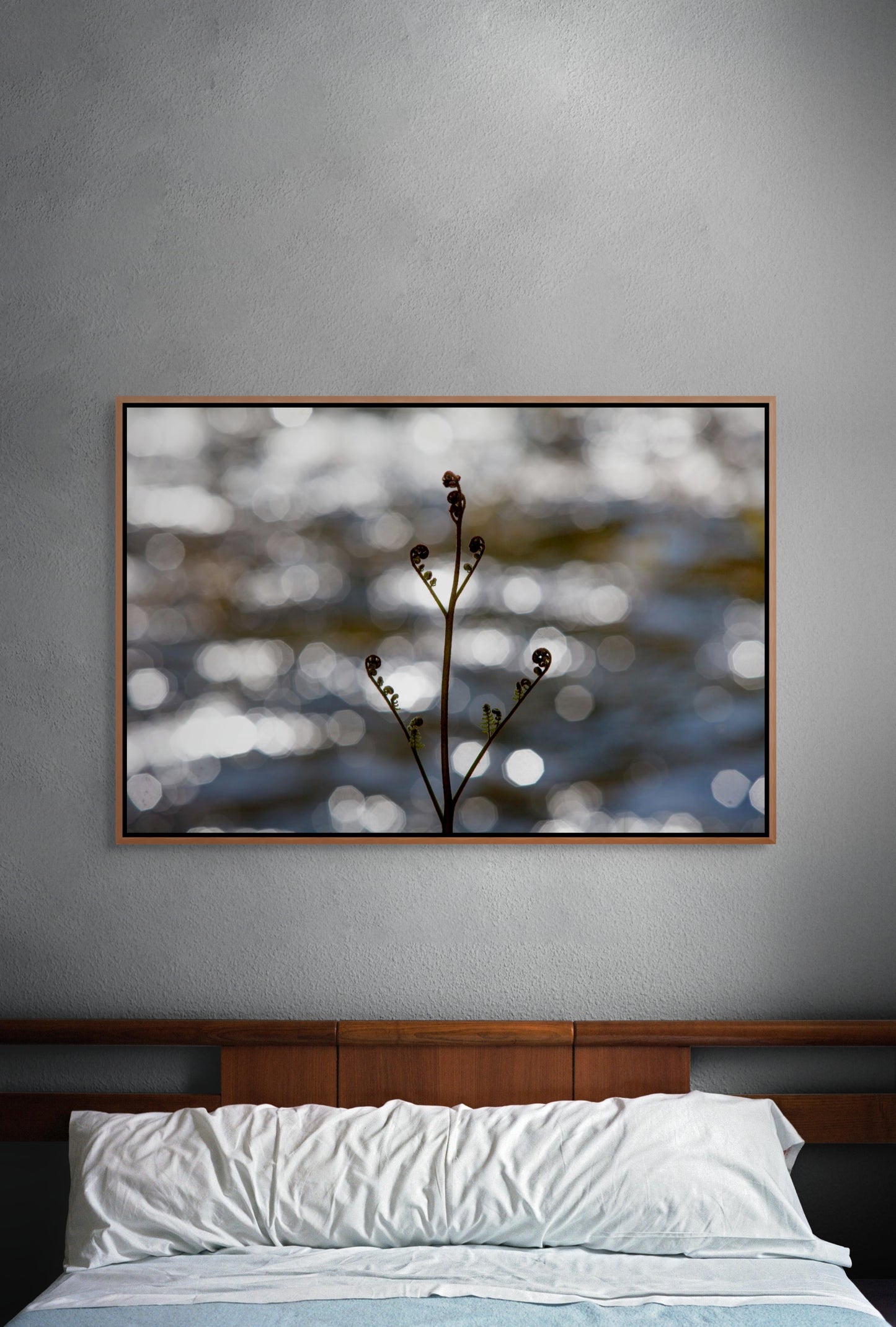 Bed with a long, single pillow and a framed artwork on a textured wall depicting a bracken fern sprouting its fronds in spring on the wall. Cedar float frame.