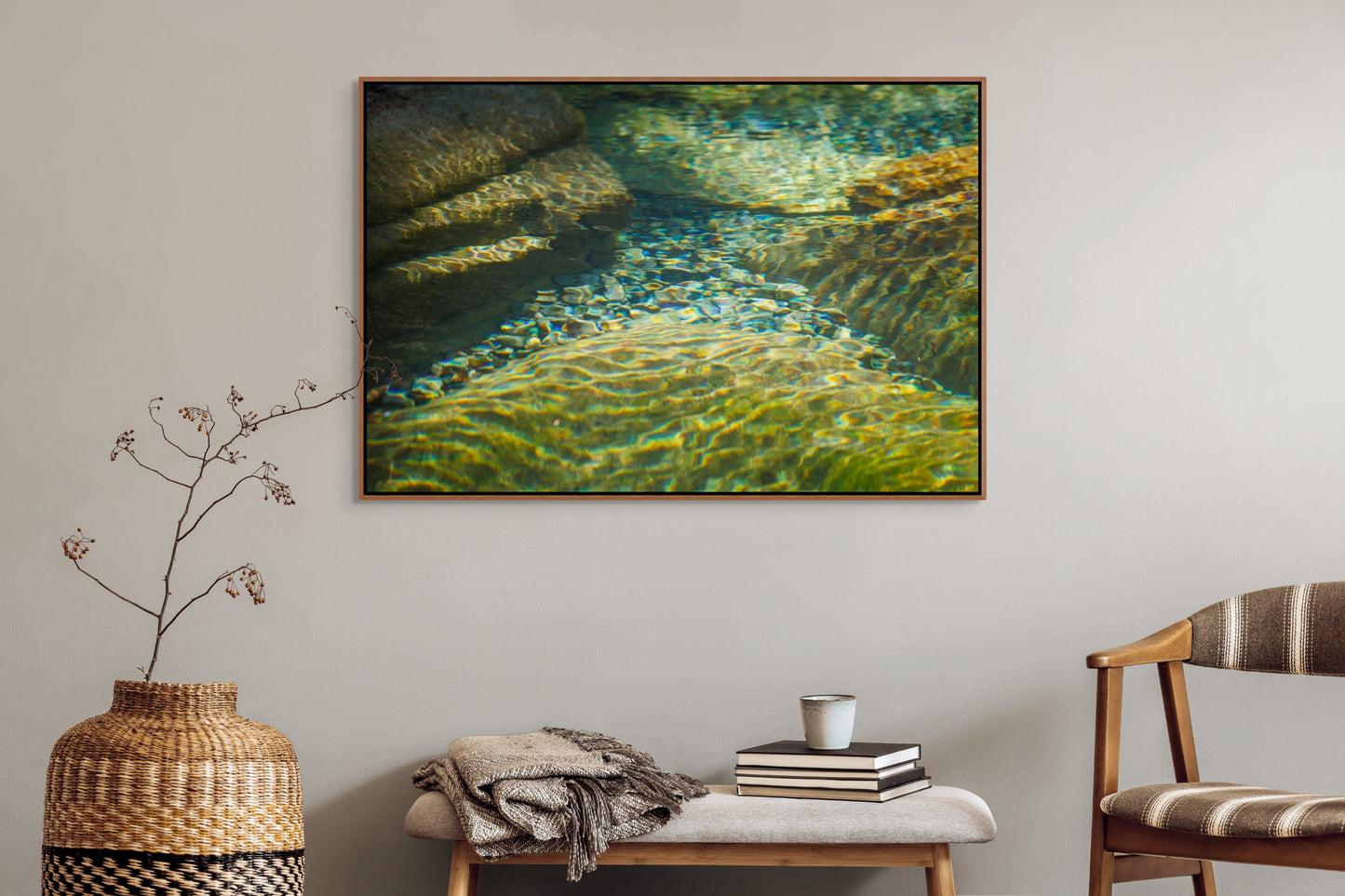 Living room with a large framed picture of clear water flowing over rocks with sunlight filtering through on the wall, a woven vase, and a chair. Cedar float frame.