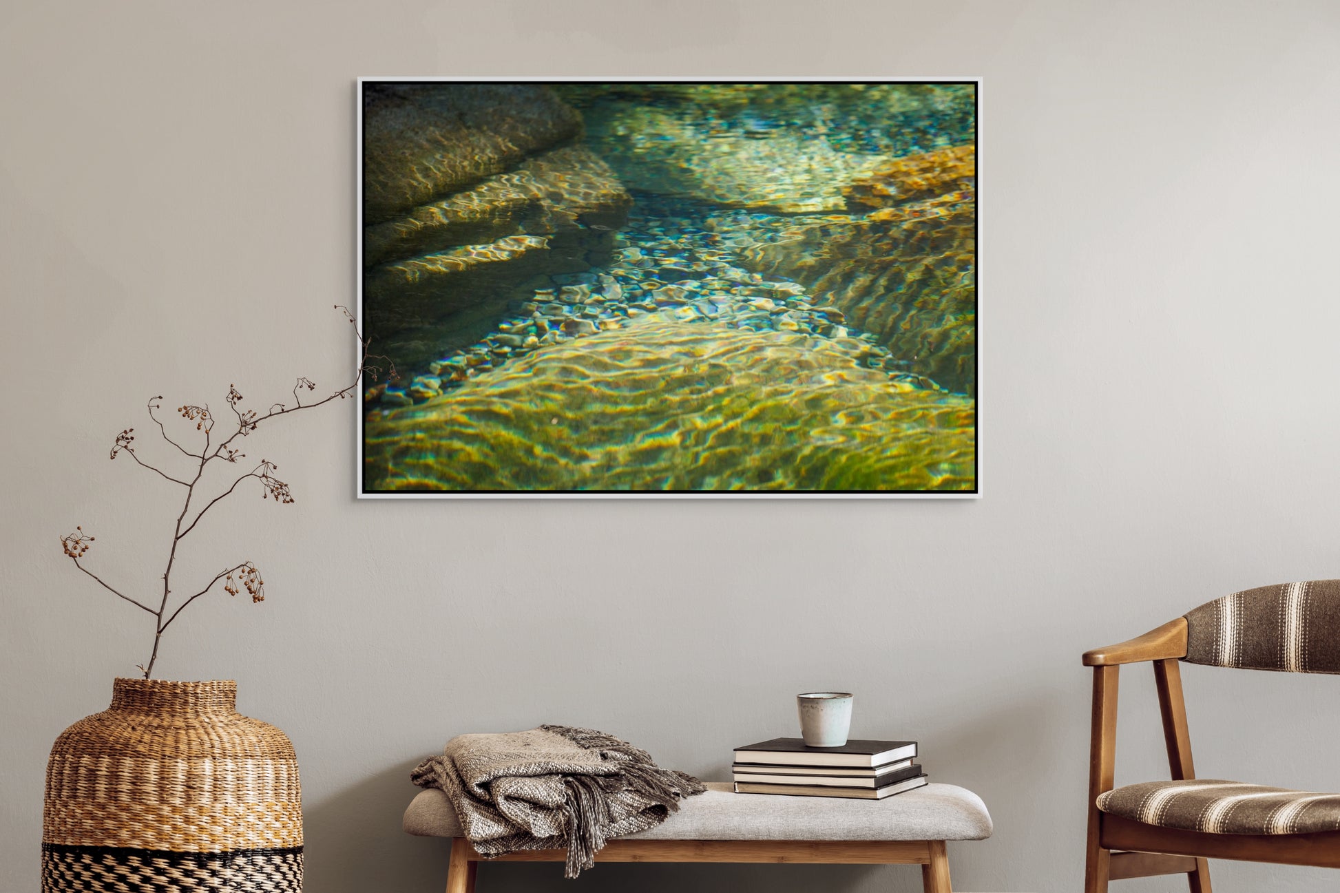 Living room with a large framed picture of clear water flowing over rocks with sunlight filtering through on the wall, a woven vase, and a chair. White float frame.